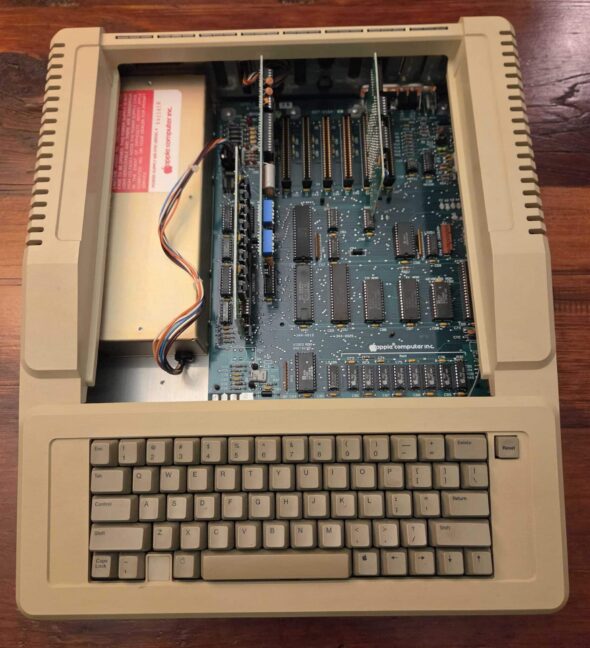 An Apple IIe with the cover removed, exposing the power supply and circuit board.