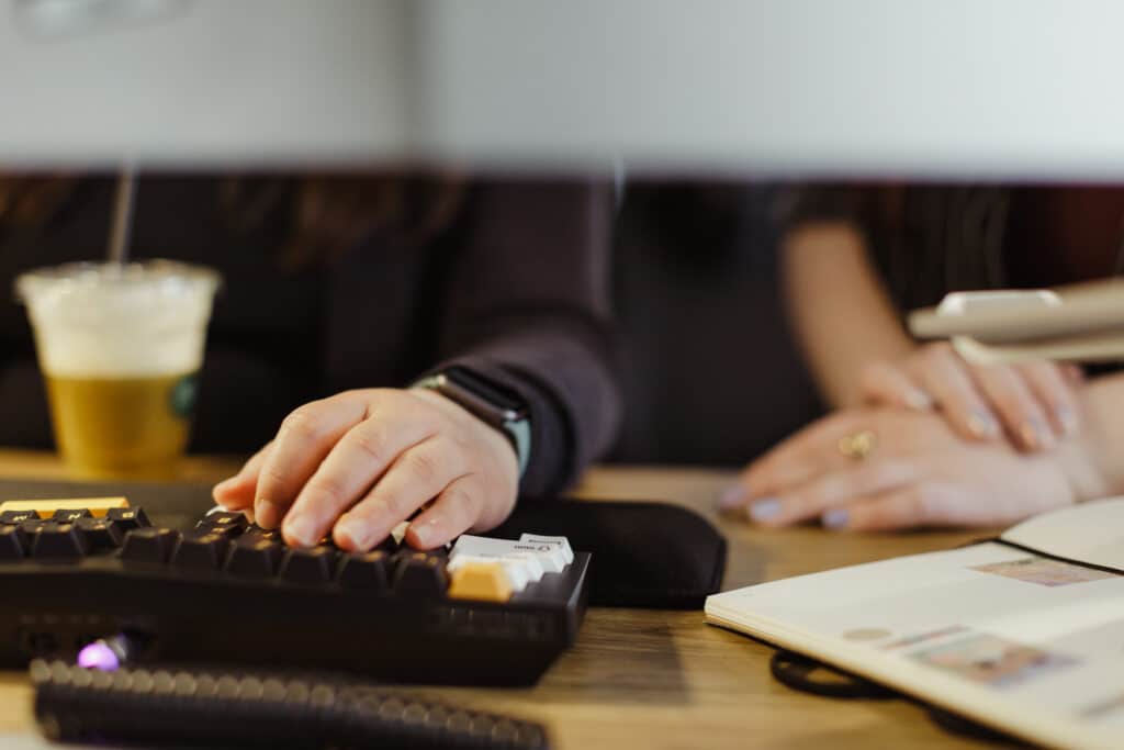 Pictured, a developer's hand on a mouse and keyboard. Post title: So You Want to Code in JavaScript: A Setup Survival Kit