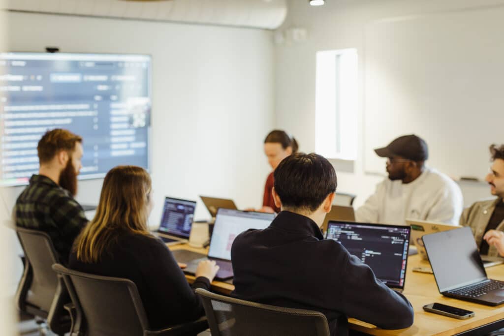 Pictured is a development team at Atomic Object's Ann Arbor office. Post title: Who Decides What's Worth Building? Growing Judgment Work Across the Team