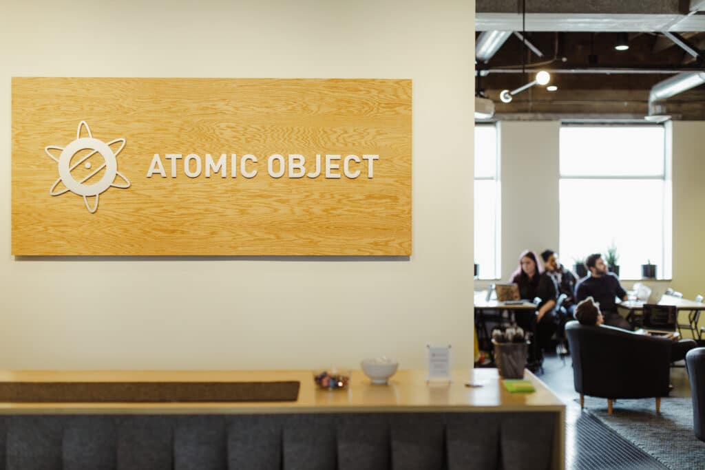 Pictured is the Atomic Object sign inside the company's Ann Arbor office. Post title: Side Projects Don't Need to Be a Grind - Let AI Do the Heavy Lifting