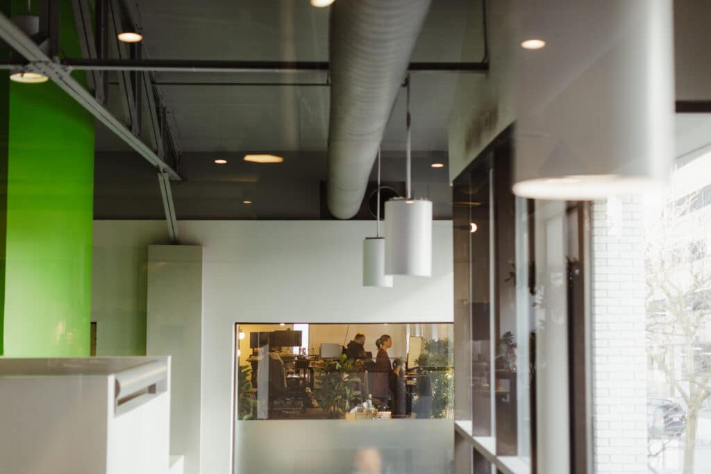 Atomic Object employees seen through a window at the Ann Arbor office. Post title: How I Use AI Before the First Line of Code