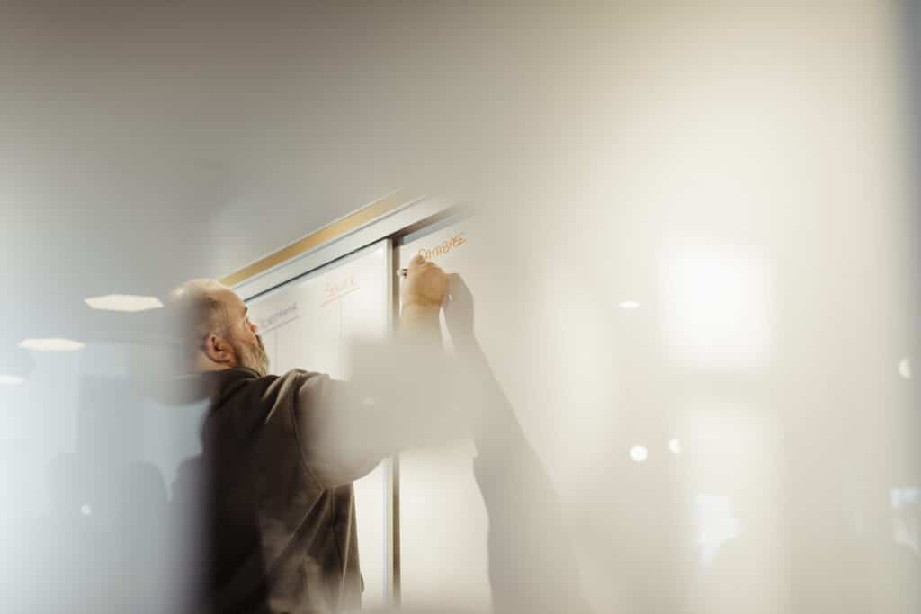 A developer writing on a whiteboard. Post title: Whiteboard Interviews: Testing for Competency, not Memorization