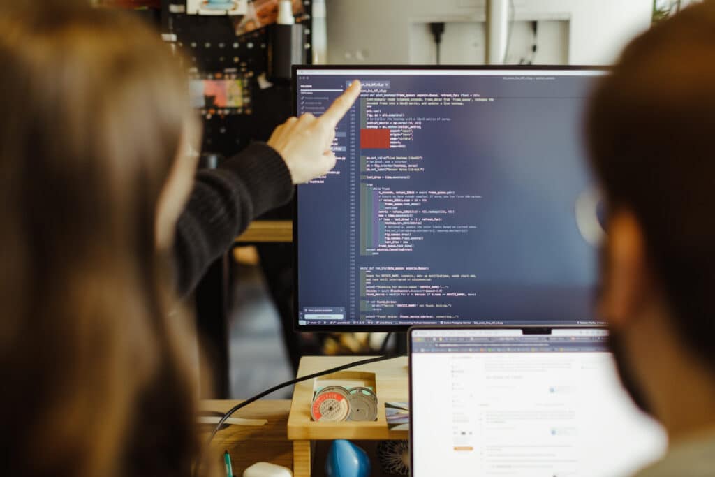 Two Atomic Object employees look at a monitor together. Post title: Even with LLMs, Let’s Pair Together