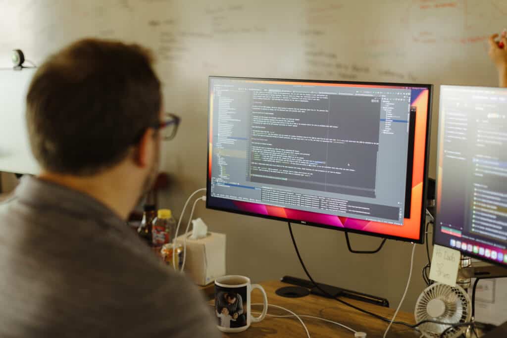 Pictured is a developer looking at code on a monitor. Post title: .NET Feature Spotlight: User-Defined Implicit Type Conversion