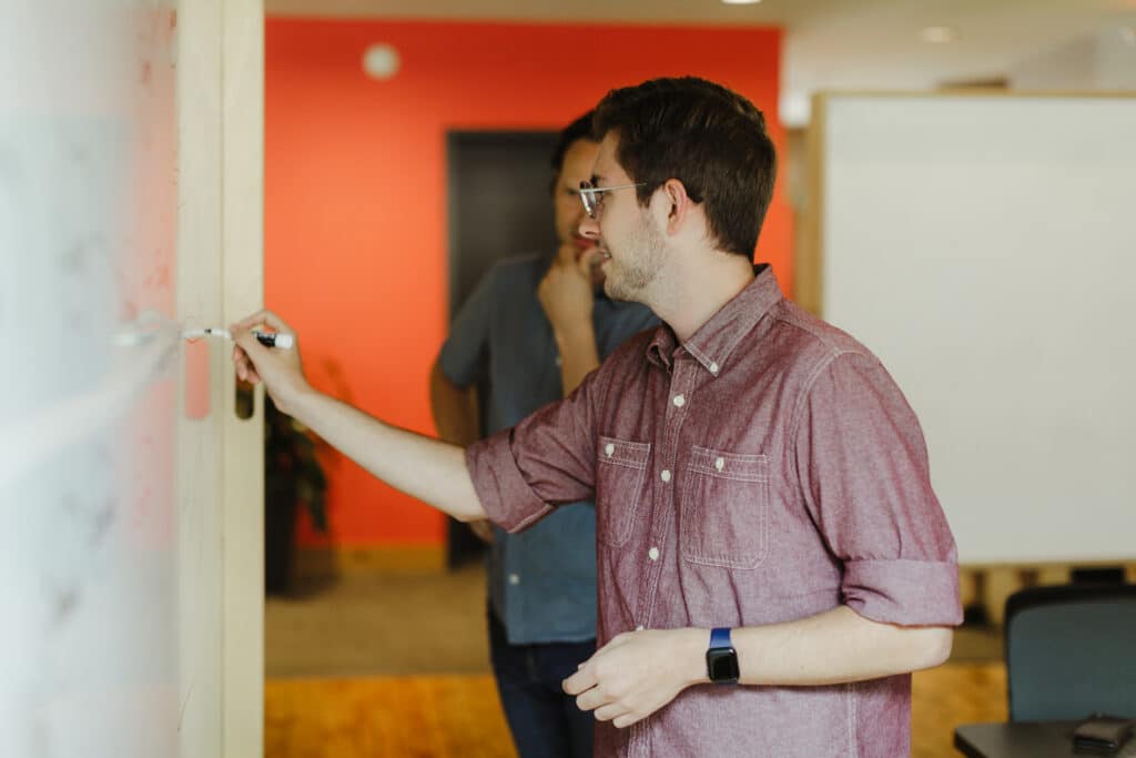 Author Jonathan Chaffer writes on a whiteboard while chatting with a co-worker. Post title: How to Manage Cognitive Load as a Developer