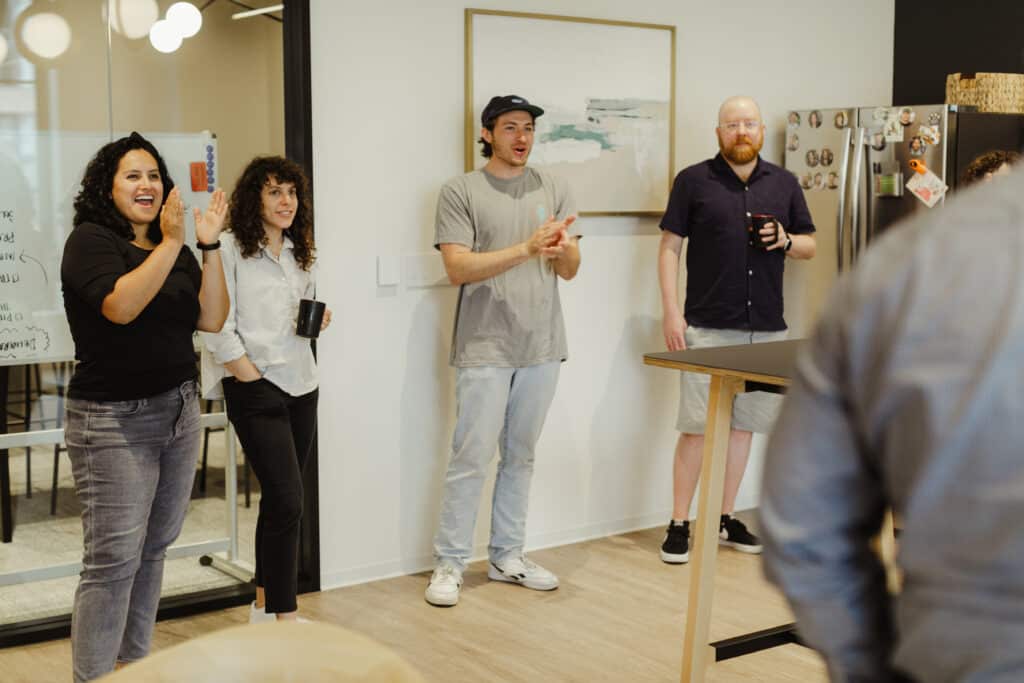 Post author Laura Corona laughs and claps with co-workers. This illustrates the post titled: People First: My Shift Toward More Meaningful Work