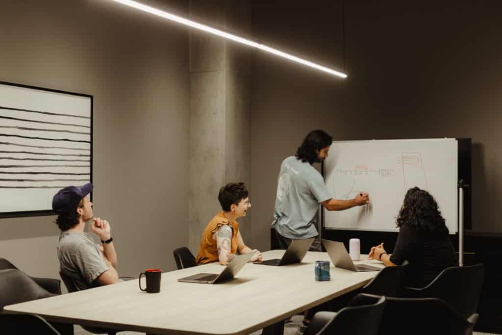 Employees of Atomic Object's Chicago office around a table in a meeting. Post title: Here's How We're Using AI Tools and What We're Learning