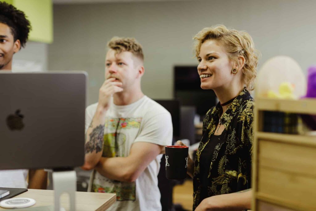 Author Casey Falkowski looks at a monitor with co-workers. Post title: TanStack Router's beforeLoad vs. loader — What's the Difference?