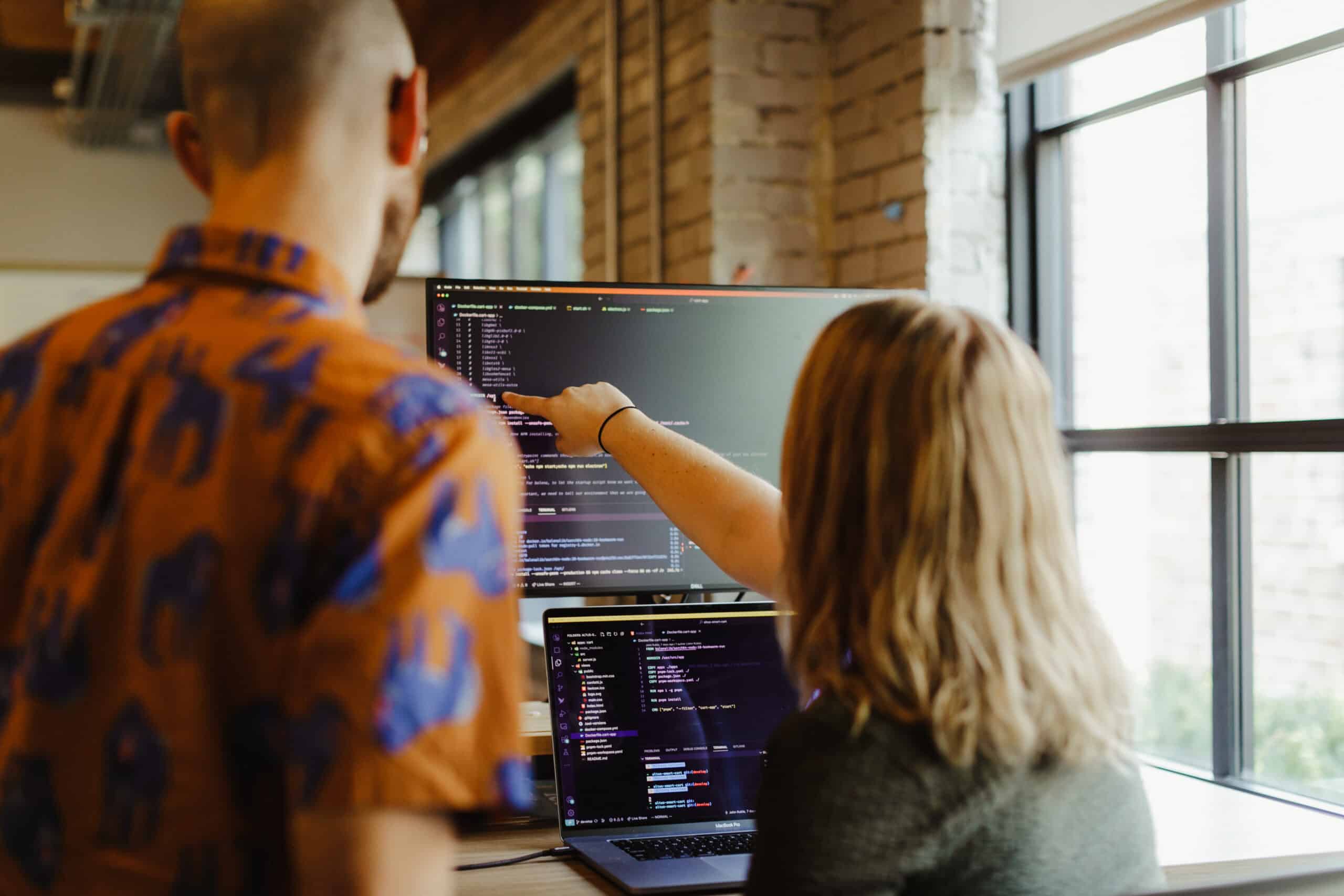 A developer gestures at a monitor while talking to her colleague. Post title: How to Prompt AI Without Handing Over Control