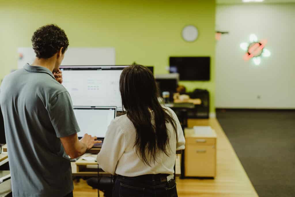 Two Atomic Object employees look at a monitor together. Post title: Notion for Multi-Office Marketing Teams: Designing for Autonomy and Alignment