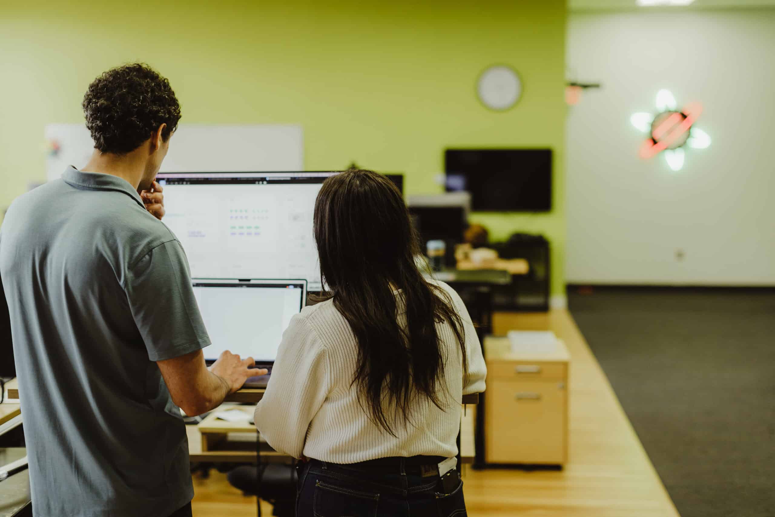Two Atomic Object employees look at a monitor together. Post title: Notion for Multi-Office Marketing Teams: Designing for Autonomy and Alignment