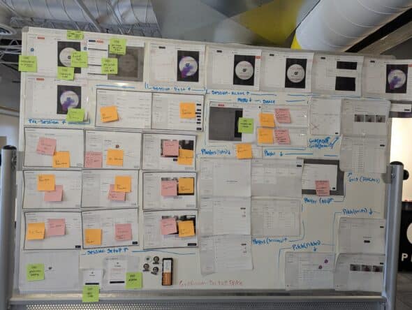 The same whiteboard but with a a few green sticky notes but the board mainly has pink and orange sticky notes in the mid section of the board on some of the designs.