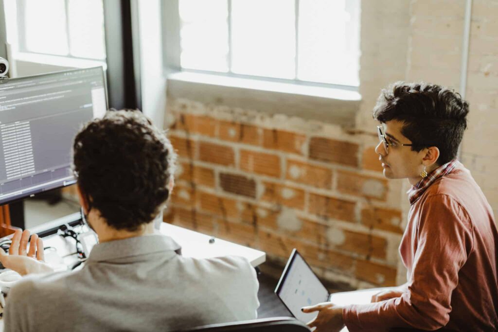 Two developers look at a monitor together. Post title: Different Ways of Leveraging AI as a Developer: Creating Developer Tools