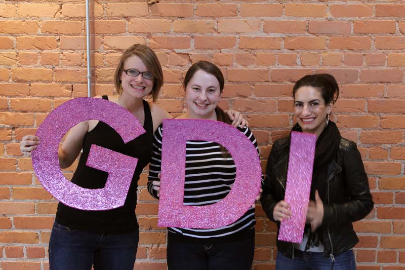 Cara Jo Miller (holding a glittery pink cardboard letter G), Erika Carlson (holding letter D), and Michelle Srbinovich (holding letter I)