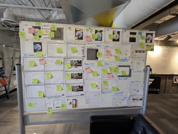 The same whiteboard but with a lot of yellow sticky notes and green covering the board. Some pink and blue sticky notes here and there.